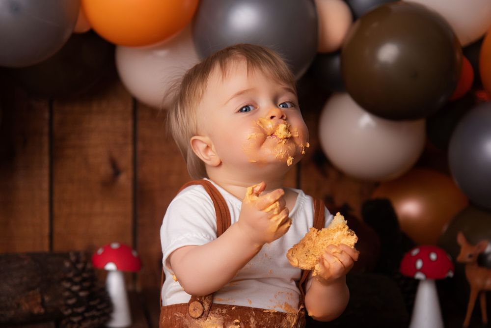 Baby cake smash photo session setup with orange and black balloons in rustic setting.