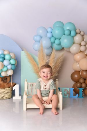 First birthday cake smash setup with blue and mint balloon garland and gold feather pampas grass decorations.