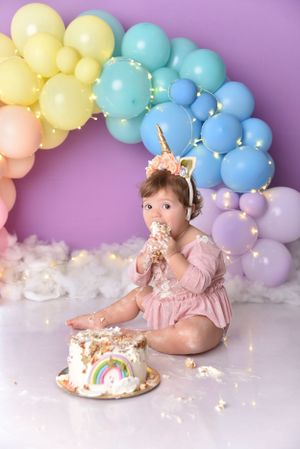 Rainbow balloon arch backdrop with pastel colors and a unicorn-themed birthday cake smash setup.