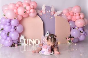 Pink and purple balloon arch with decorative panels creates dreamy first birthday photo setting.
