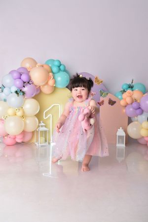 First birthday celebration setup with pastel balloon arch and baby in pink tulle dress.