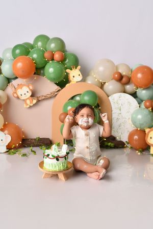 Safari theme cake smash setup with green and orange balloon garland and animal decorations.