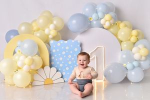 First birthday photo setup with blue and yellow balloon arch and polka dot decorations.