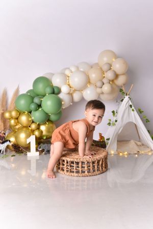 Birthday photo setup with teepee, balloon garland, and small child on wicker ottoman.