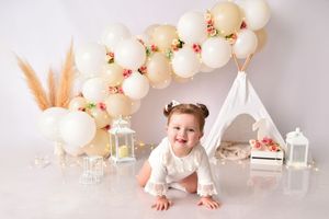 Birthday photo backdrop with cream balloon garland, teepee, and lantern decorations.