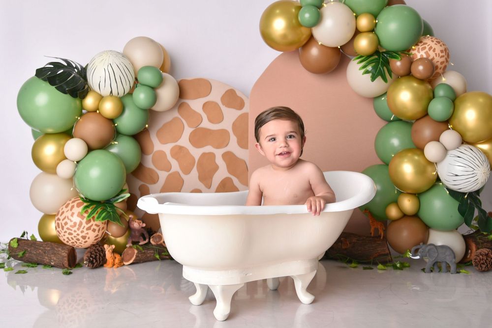 Safari-themed balloon arch with green and gold decor surrounding a vintage bathtub photo setup.