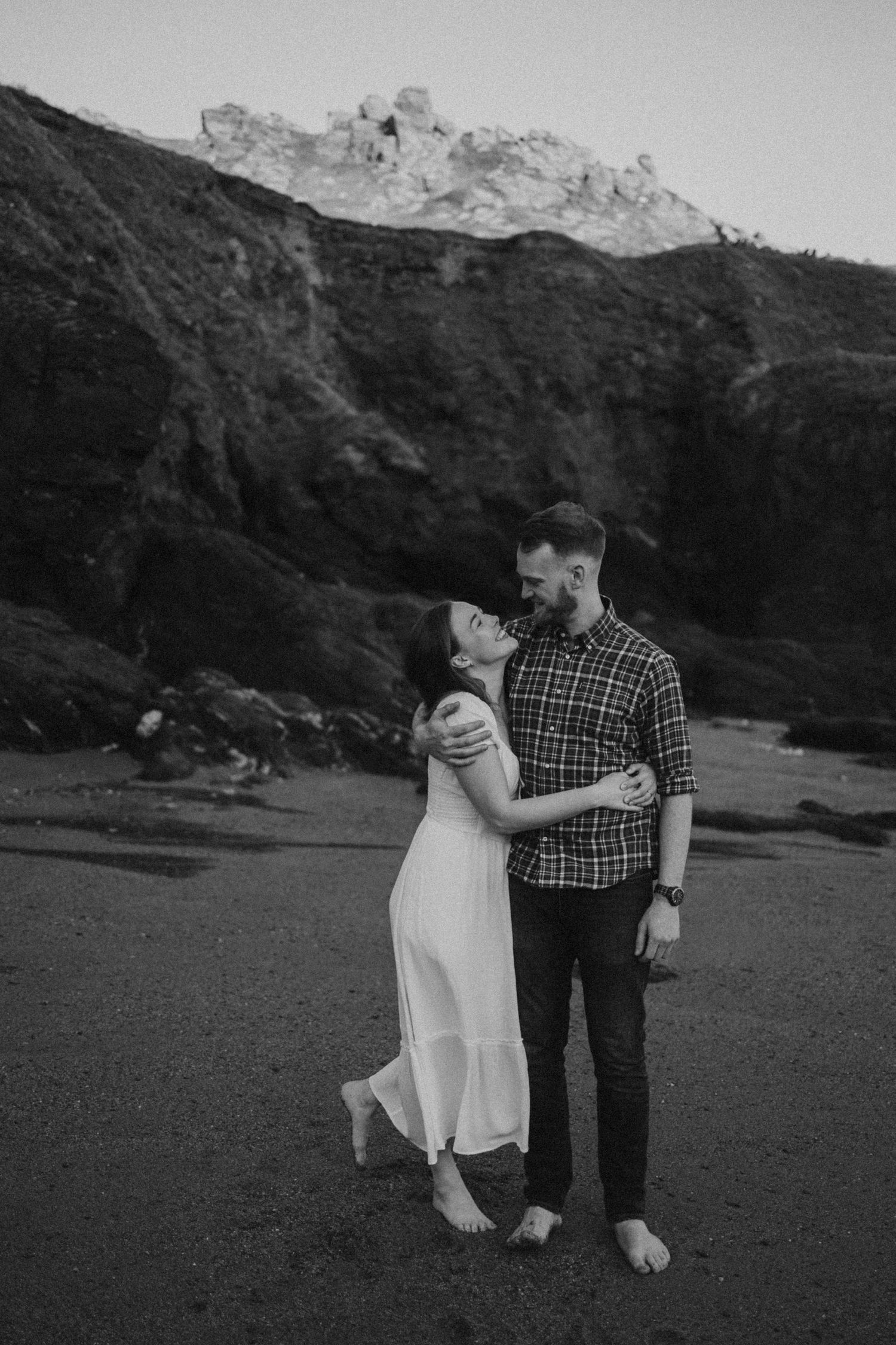 A couple embraces on a beach with dramatic Devon cliffs in the background, South Hams, Devon.