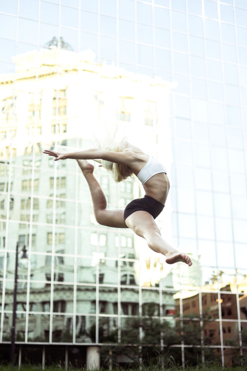 Dancer leaps gracefully through the air against modern city architecture.
