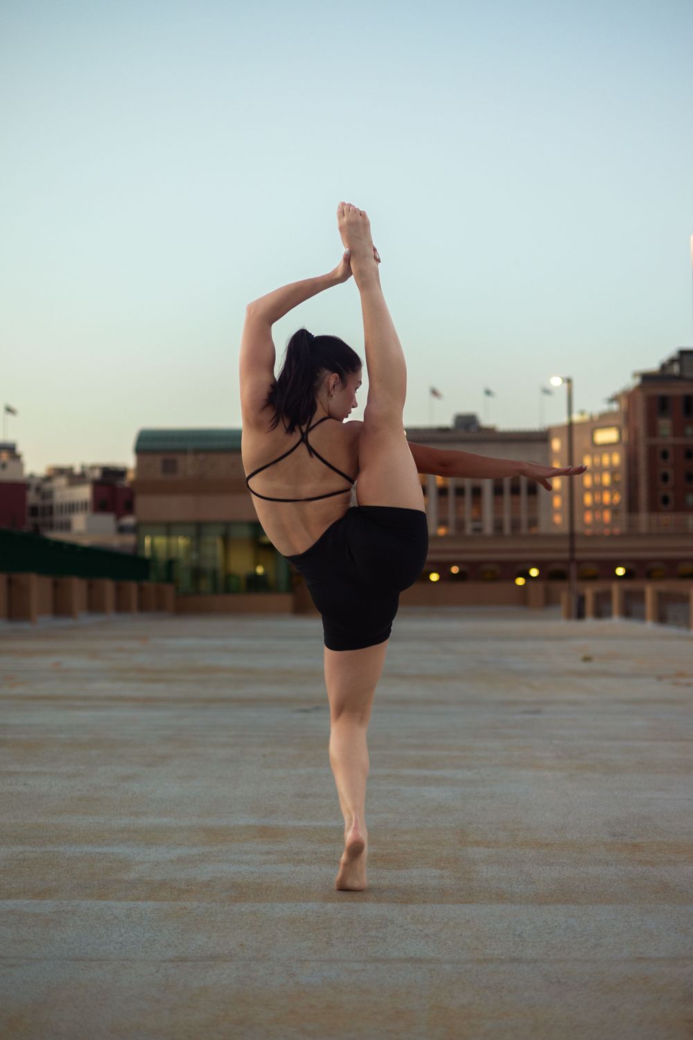 Silhouetted dancer performing splits on rooftop during sunset.