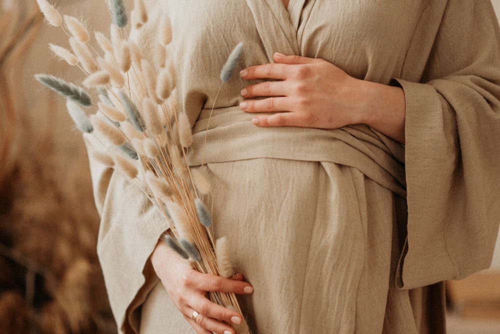 Artistic maternity photos showing hands holding dried flowers against neutral beige clothing.