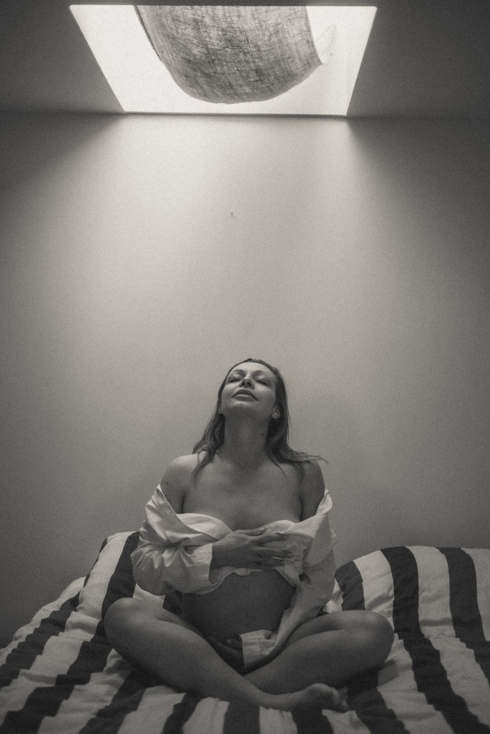 Black and white sequence of person resting on striped bedding under skylight.