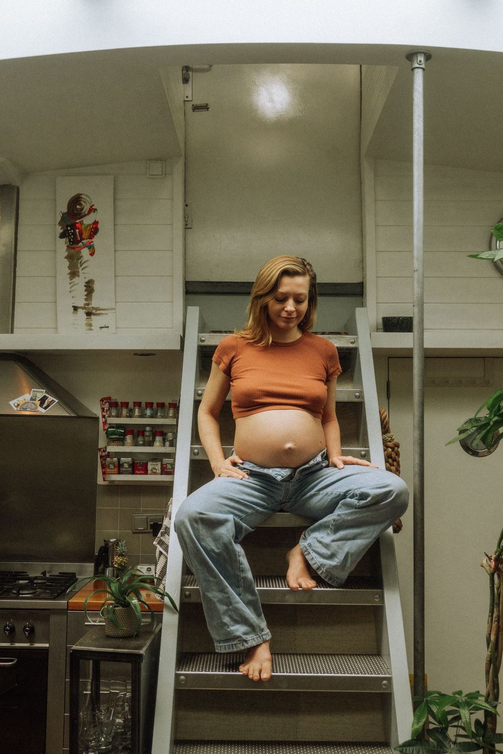 Casual indoor portrait showing someone sitting on a counter wearing an orange top and jeans in a kitchen setting.