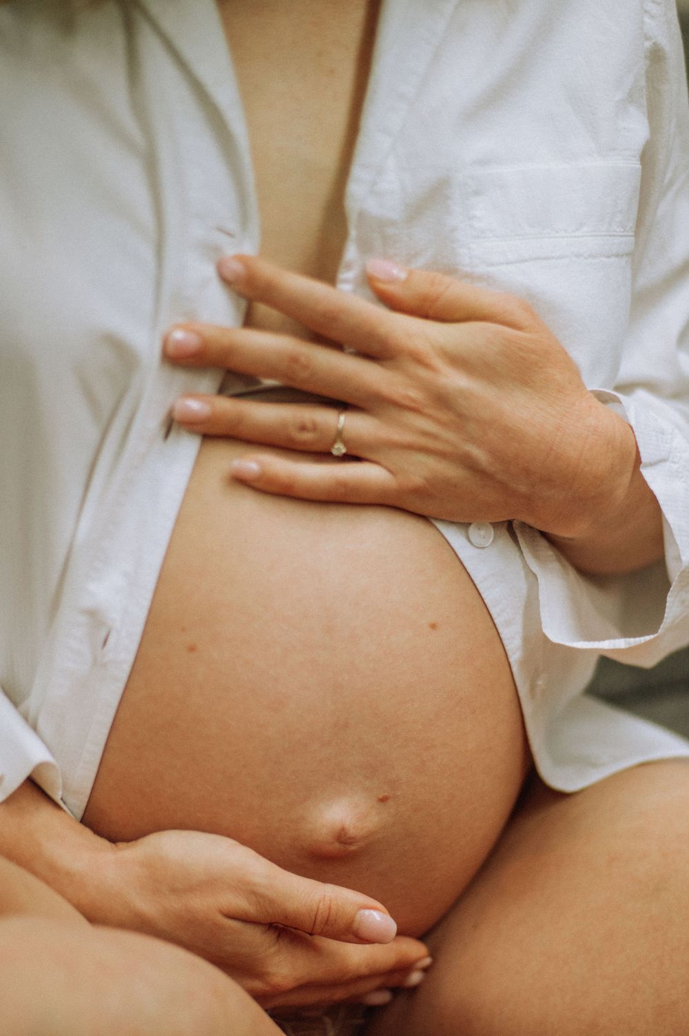 Close-up shots of hands gently cradling a pregnant belly in a white shirt.