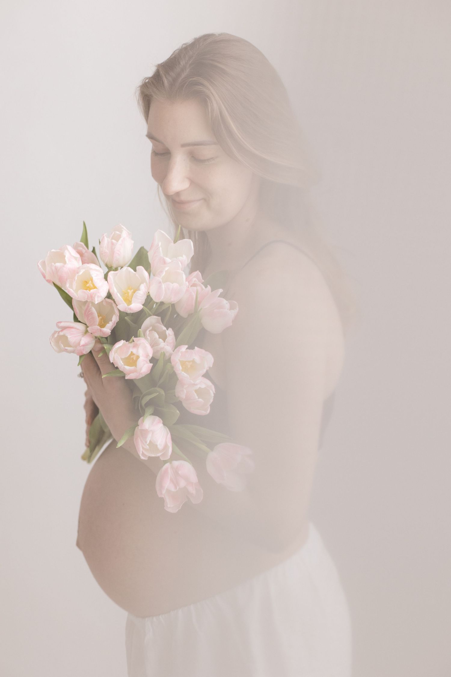 Artistic maternity portrait with flowing white fabric against light background.