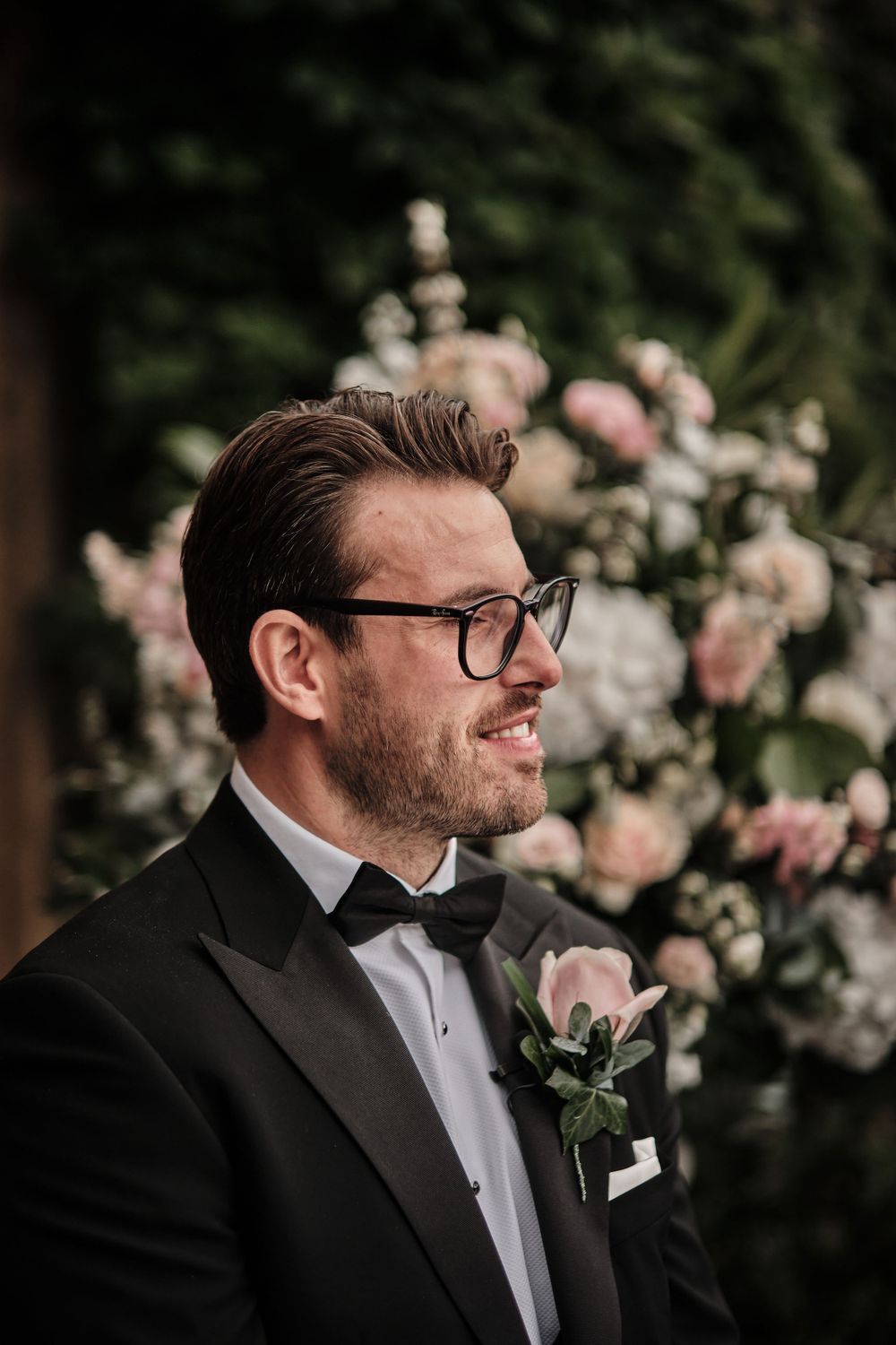 Elegant wedding attire with formal black tuxedo and bow tie against a backdrop of pink roses.