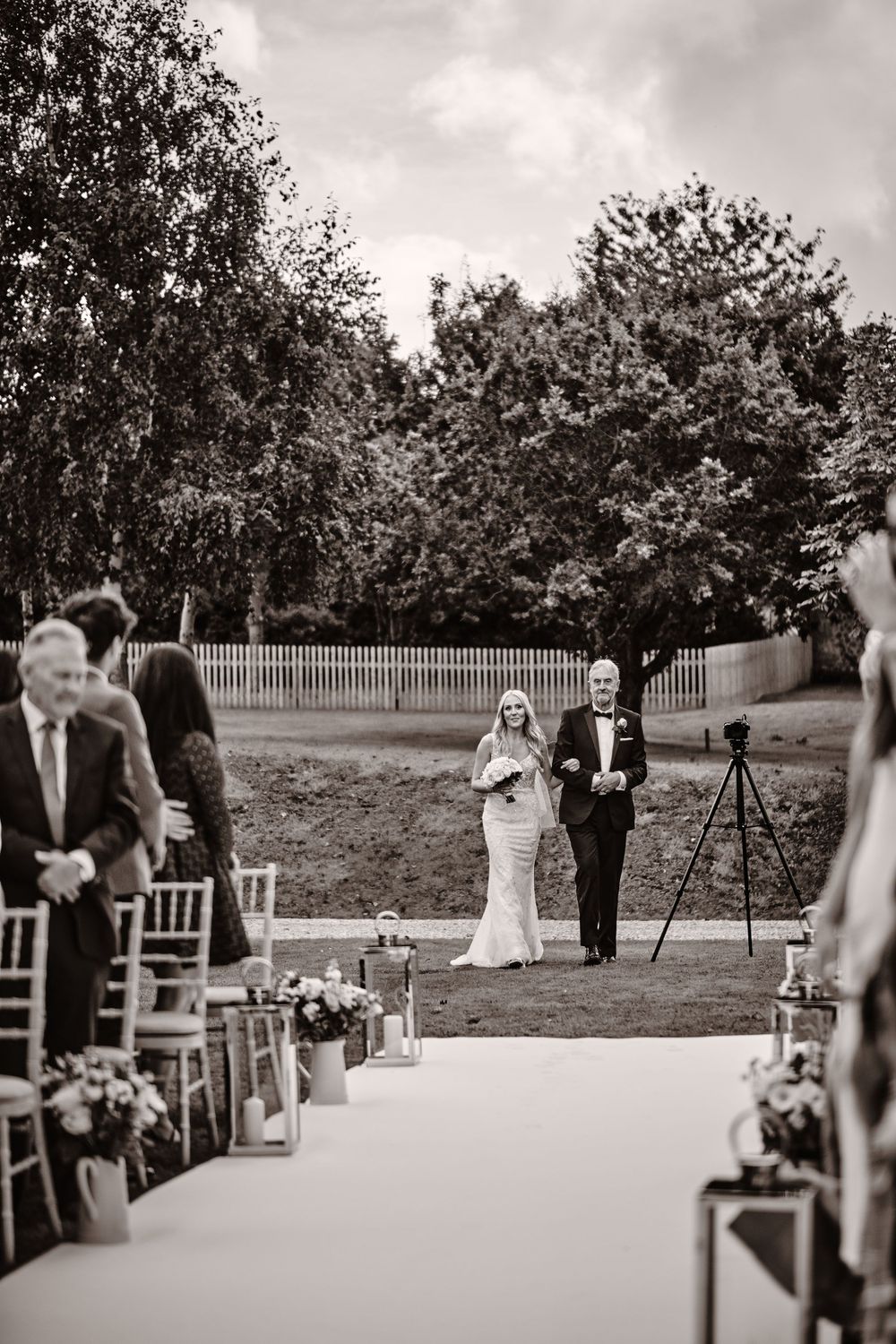 Black and white photo of wedding ceremony with white aisle runner leading to outdoor altar.