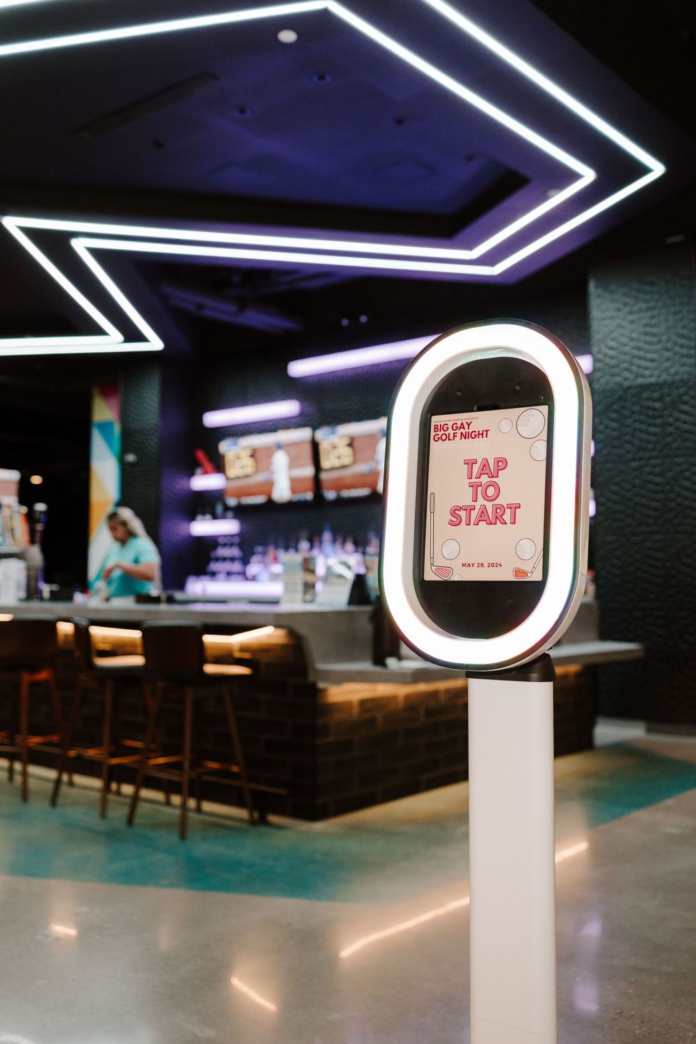 Modern bar interior with geometric LED lighting and a 'Tap to Start' digital kiosk display.