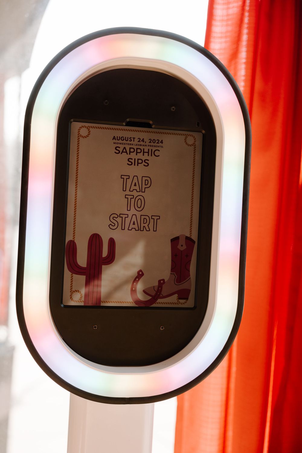 Photo booth screen displaying 'Sapphic Sips Tap to Start' with cactus graphics and LED frame.