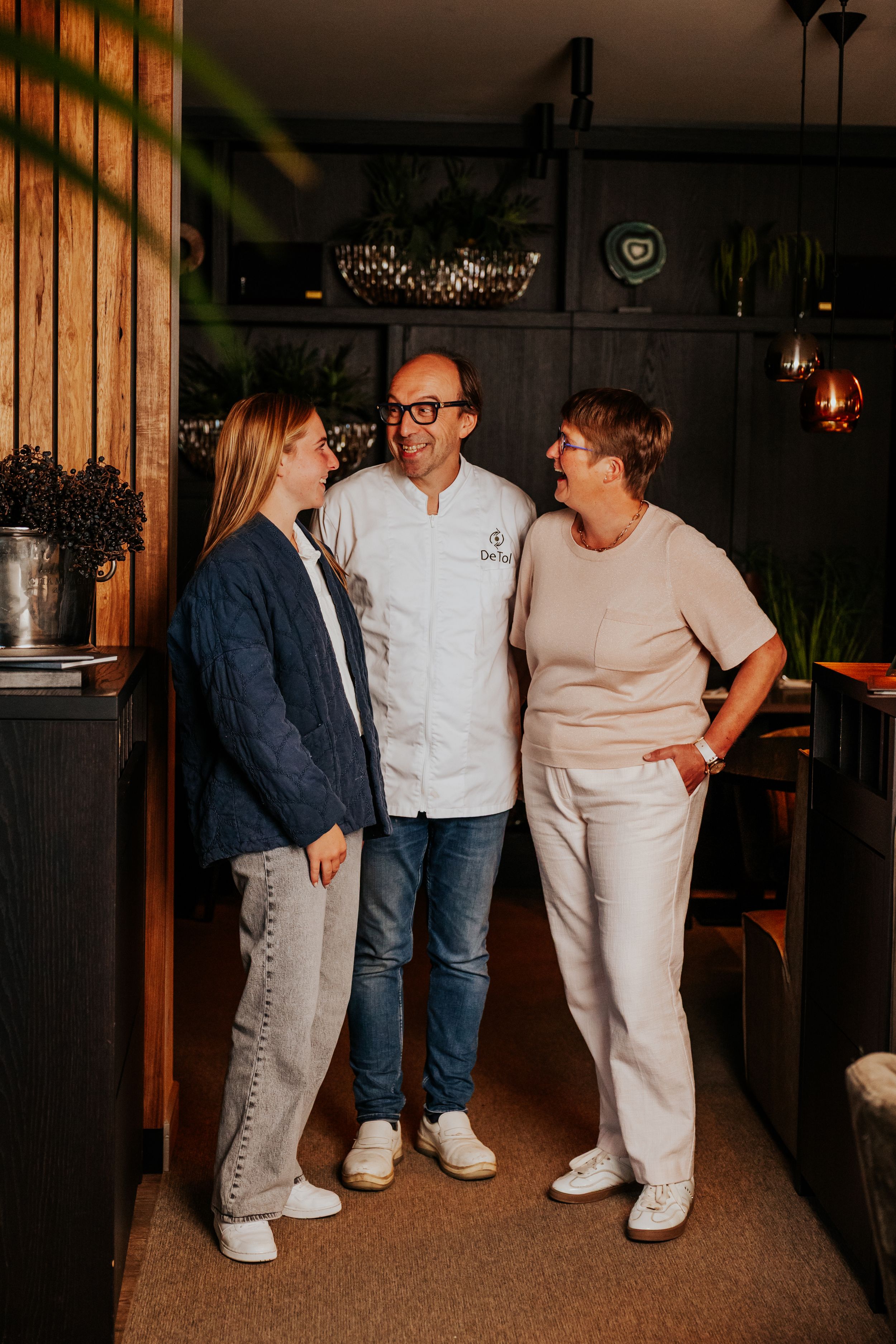 Group of people in casual attire standing together in cozy indoor setting with wooden decor.