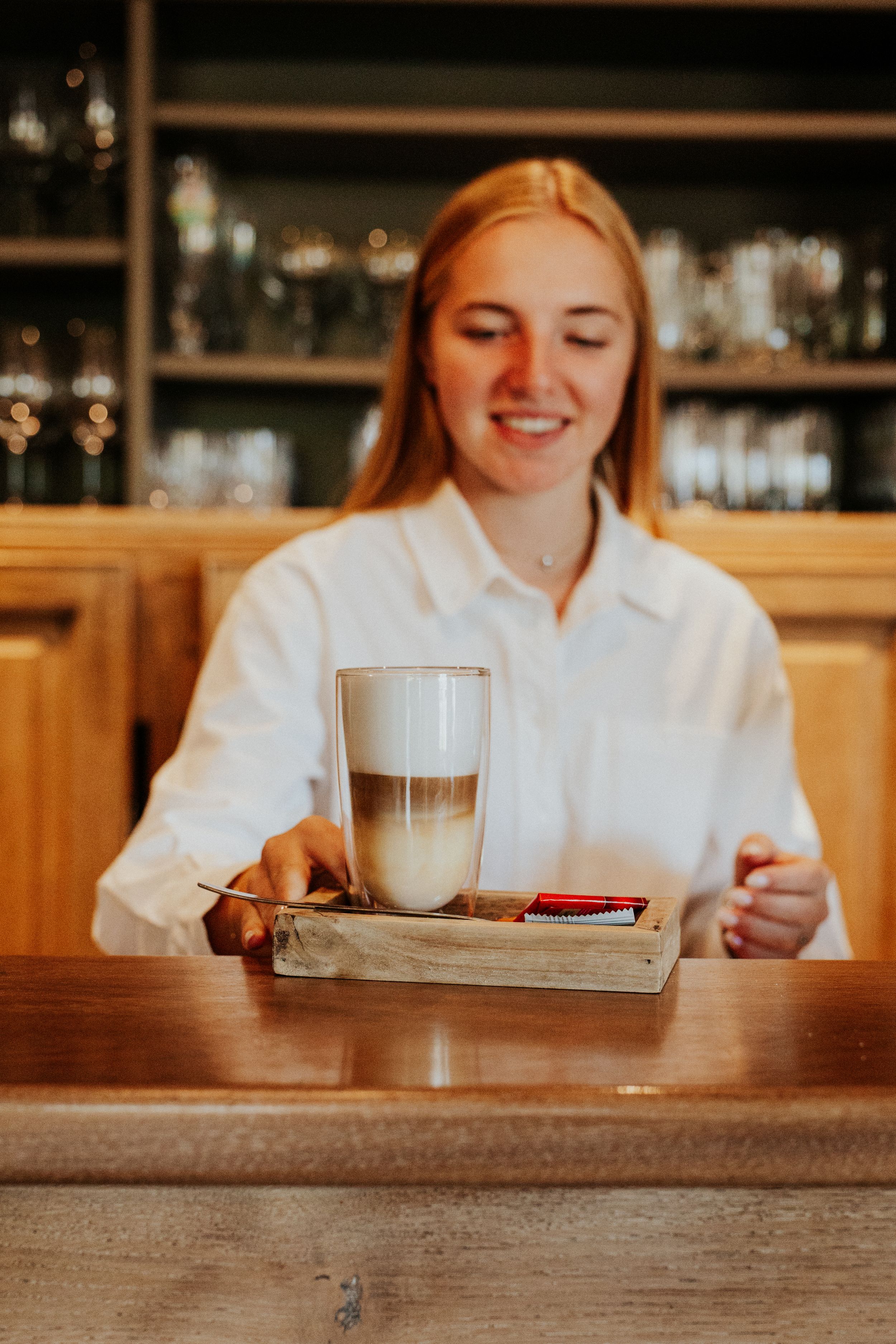 Person in white shirt sitting at wooden bar counter with beverage.