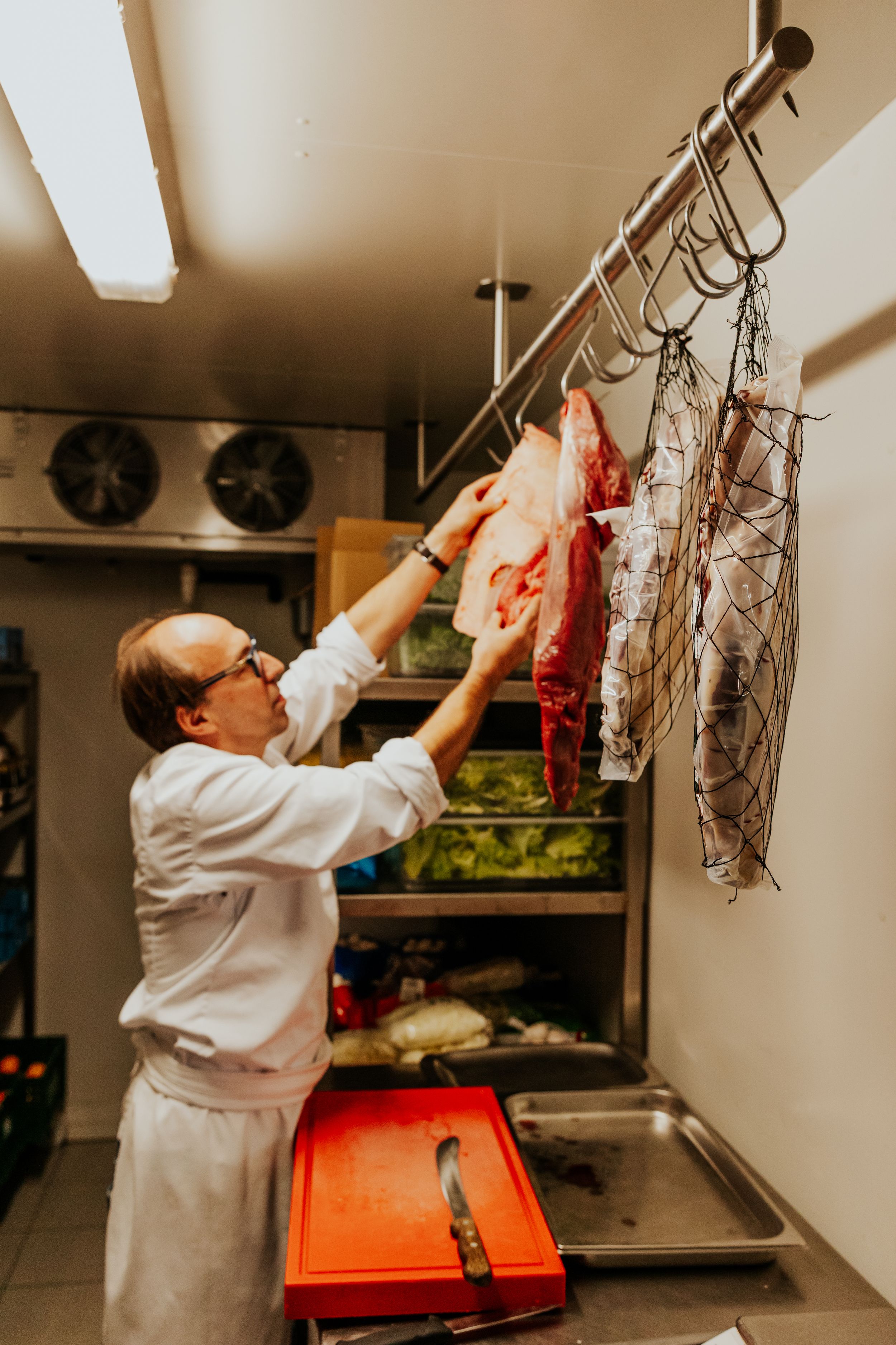 Chef in white uniform handling meat products in commercial kitchen setting.