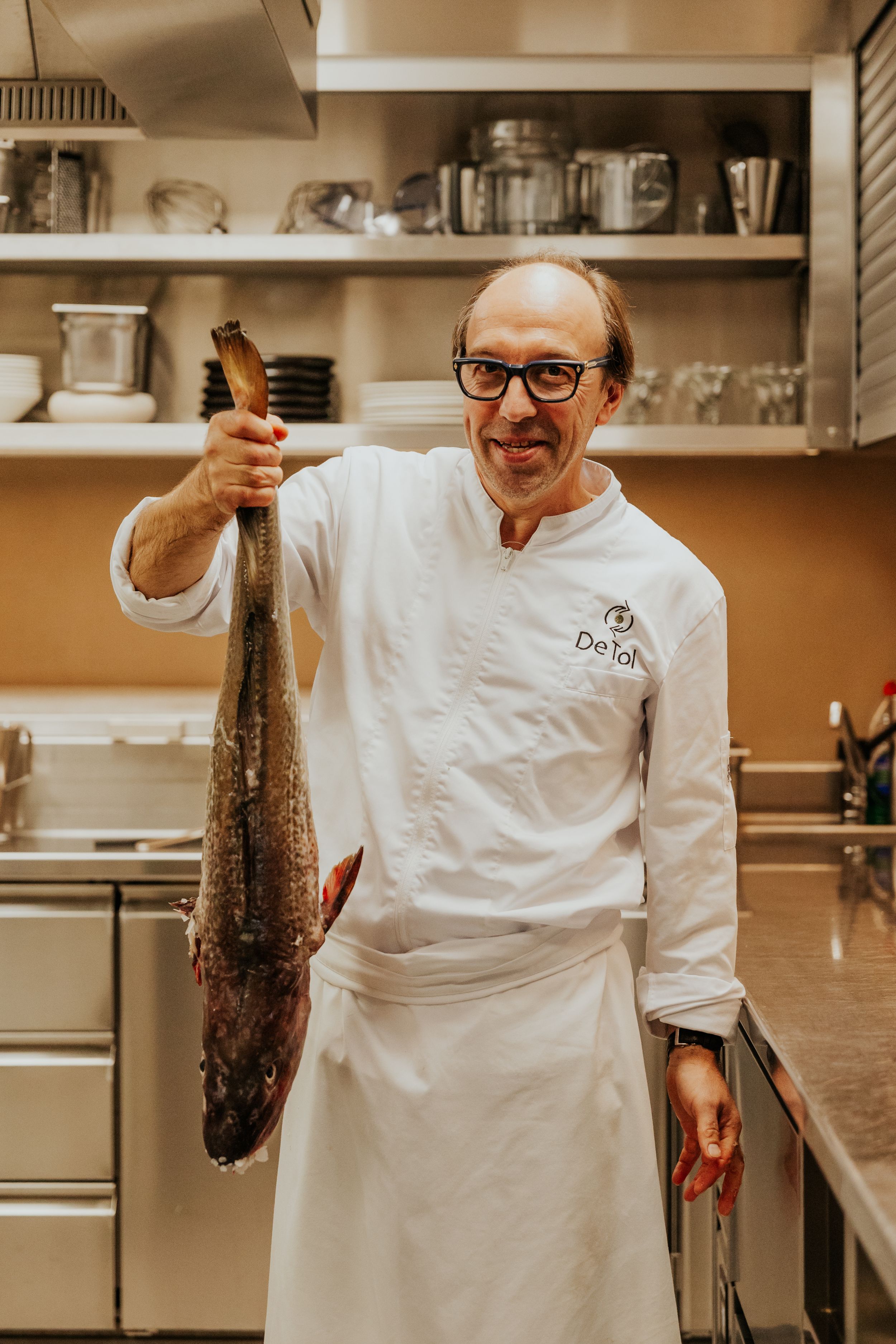 Chef in white uniform proudly displaying fresh fish in professional kitchen.