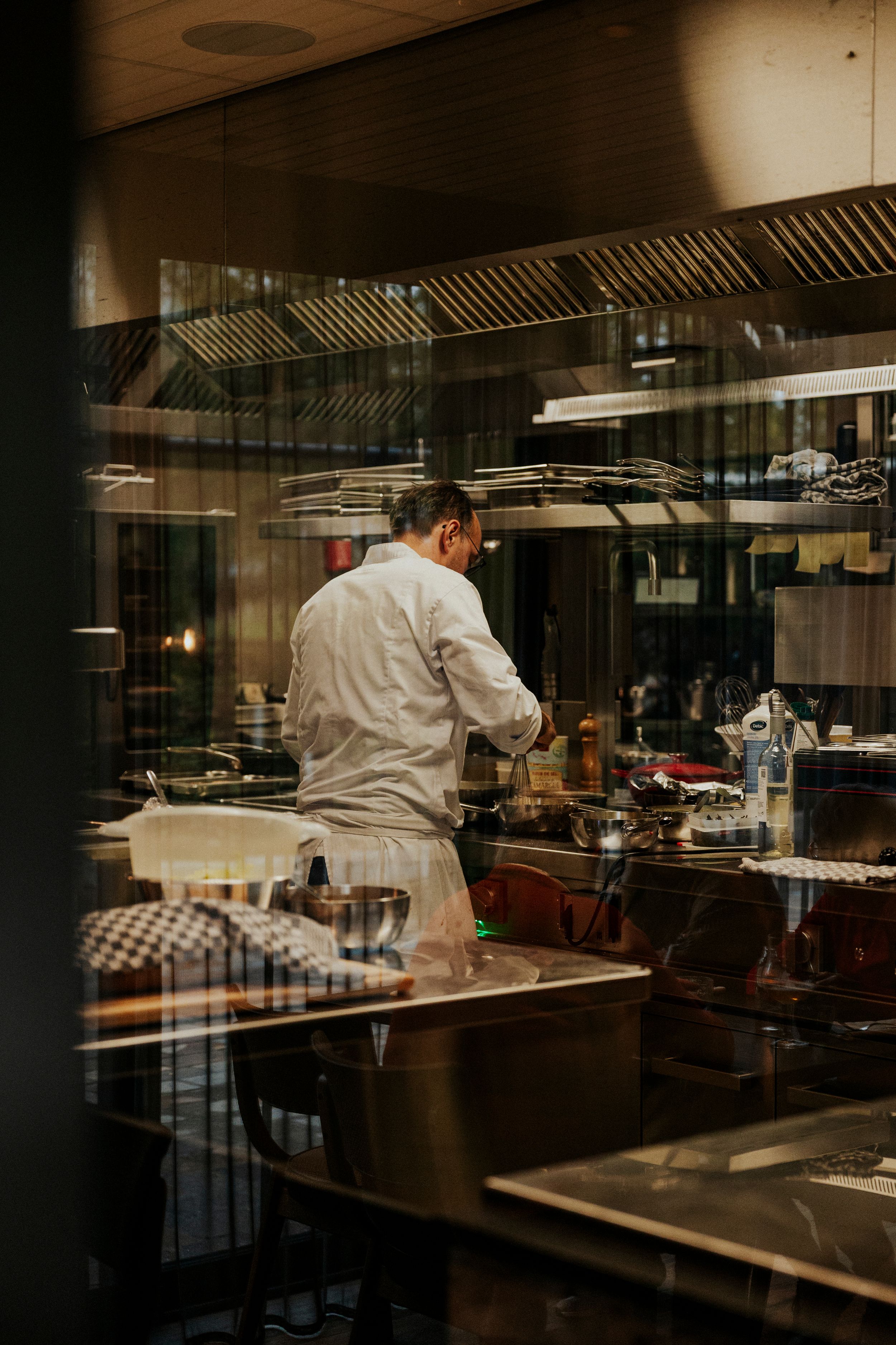 Professional kitchen interior with chef working at stainless steel counters in dim lighting.