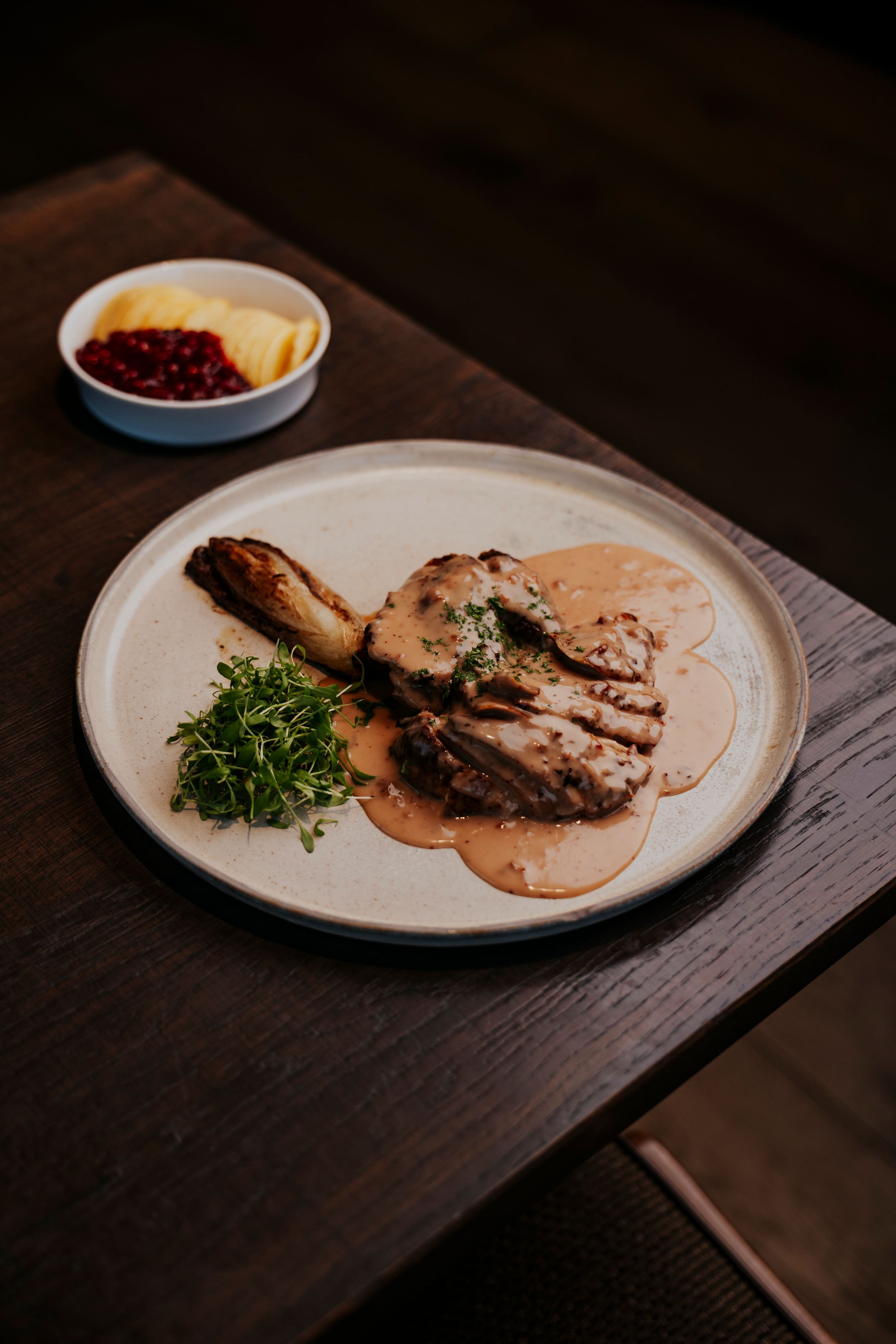 Plated meat dish with garnish and sauce served on dark wooden table in restaurant setting.