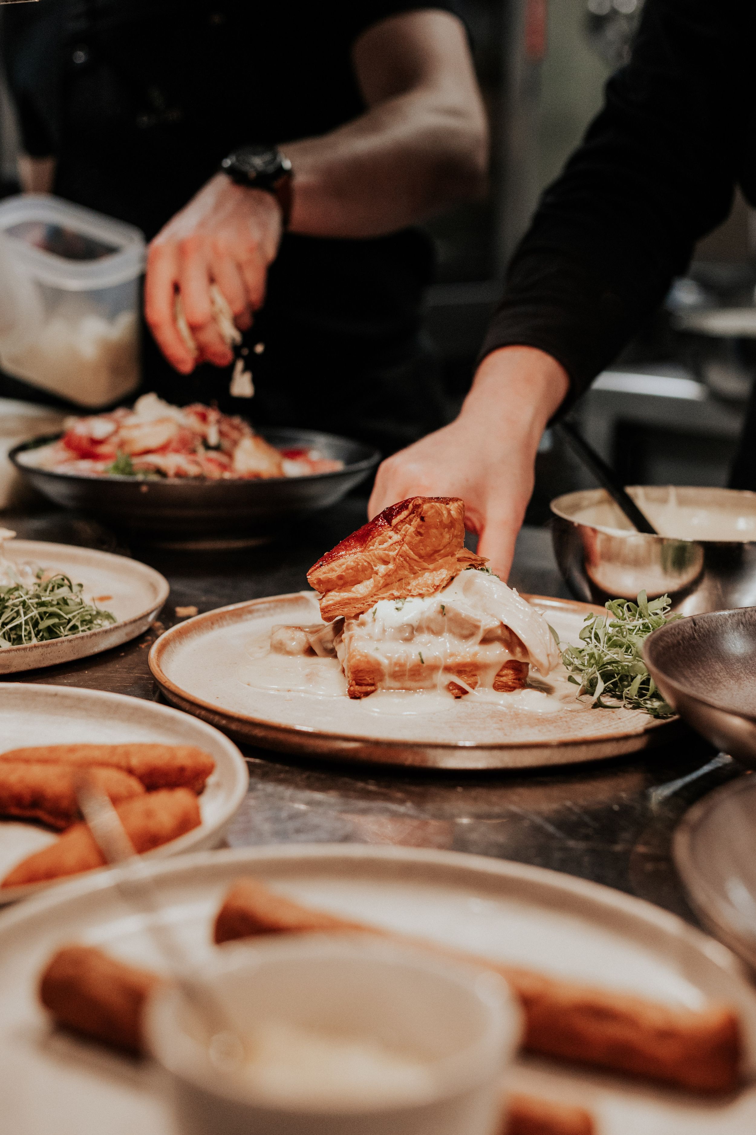 Hands plating food in a professional kitchen setting.