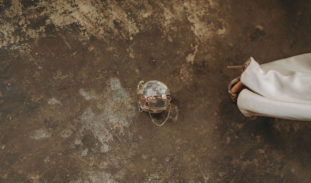 Gold coloured spherical handbag on a concrete floor with foot of guests in view. Editorial wedding