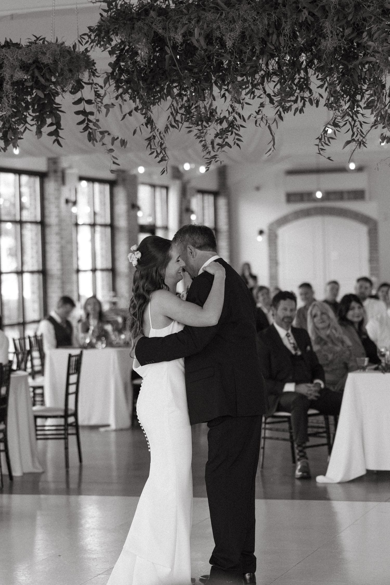 Elegant bride in white dress seated at decorated head table in black and white.