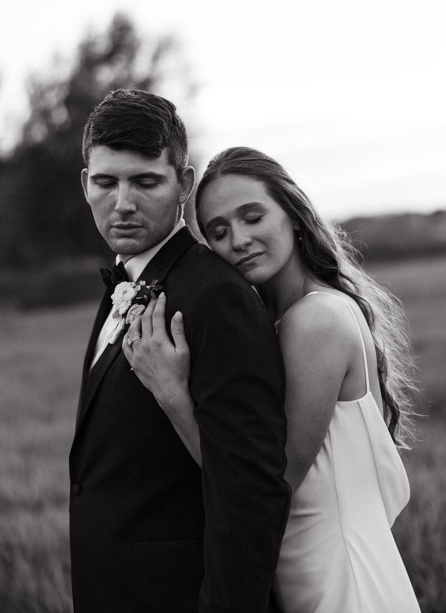 Intimate black and white portrait of newlyweds embracing in outdoor field setting.