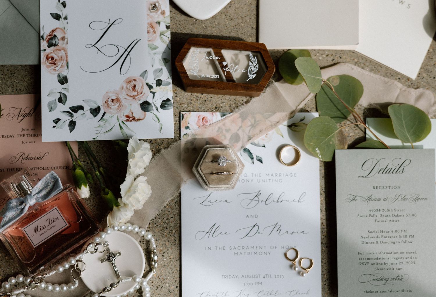 Wedding invitation suite with floral designs, rings, and delicate accessories on a rustic surface.