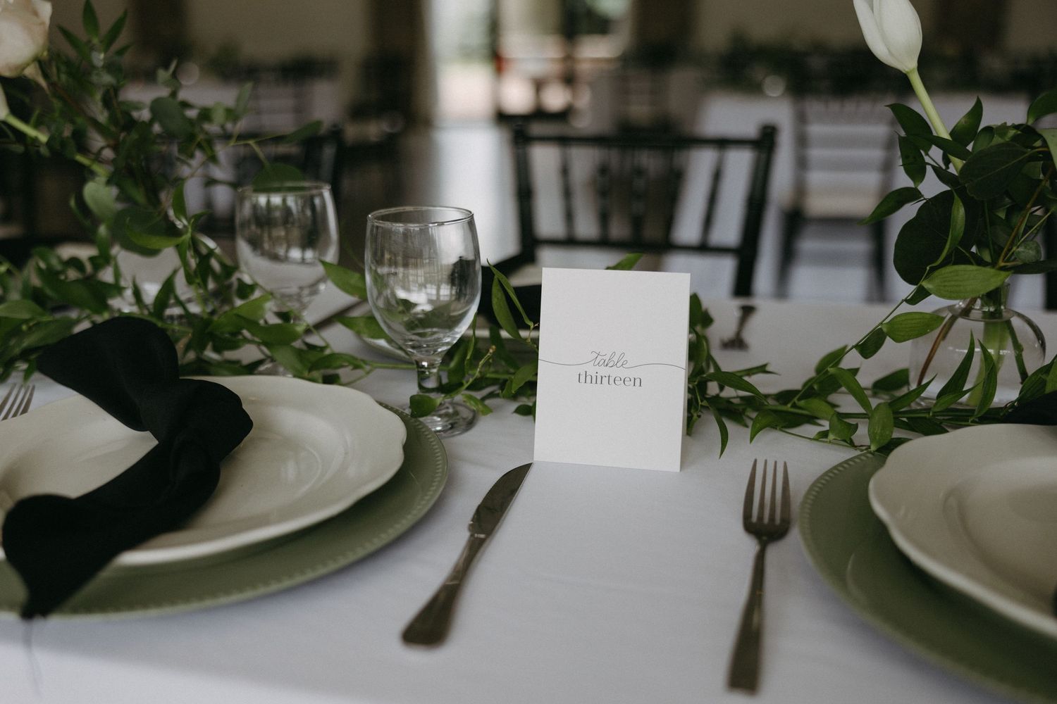 Elegant table setting with white plates, green napkins and botanical decorations at a wedding reception.