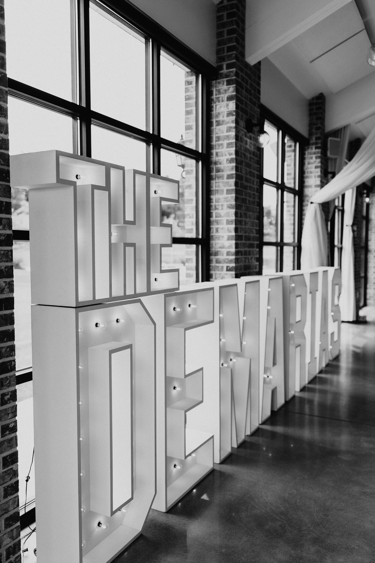 Modern industrial hallway with large white illuminated letters against exposed brick walls.