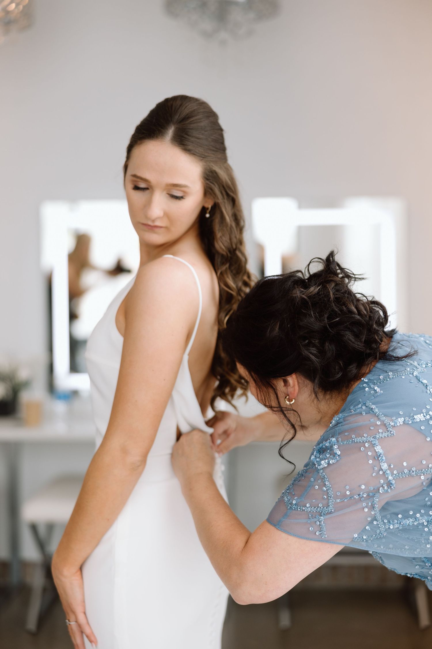 Wedding dress preparation moment in a brightly lit dressing room.