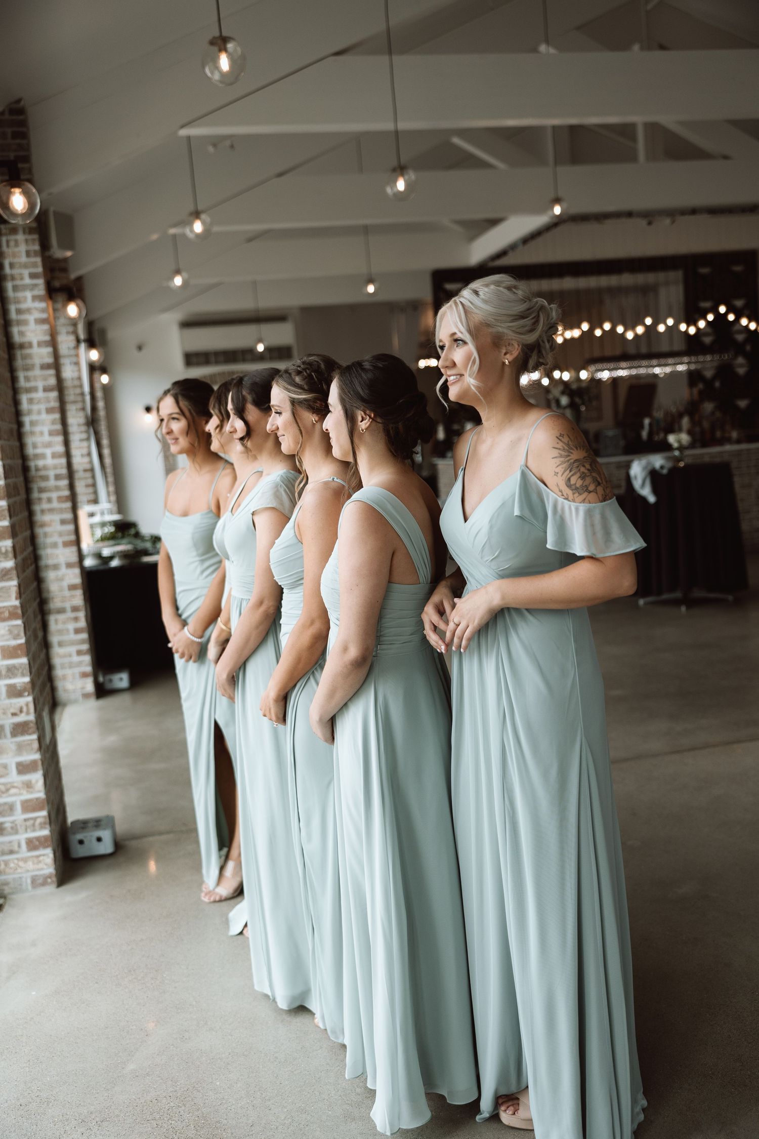 Bridesmaids in light blue dresses lined up in an industrial style venue.