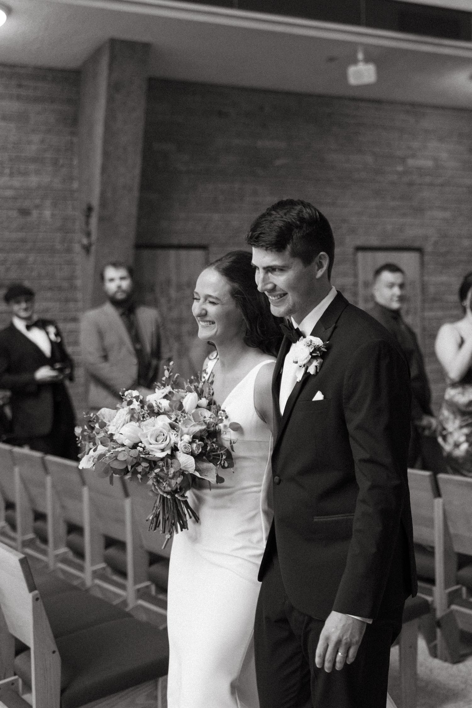 Black and white photo of newlyweds sharing joyful moment during church ceremony.