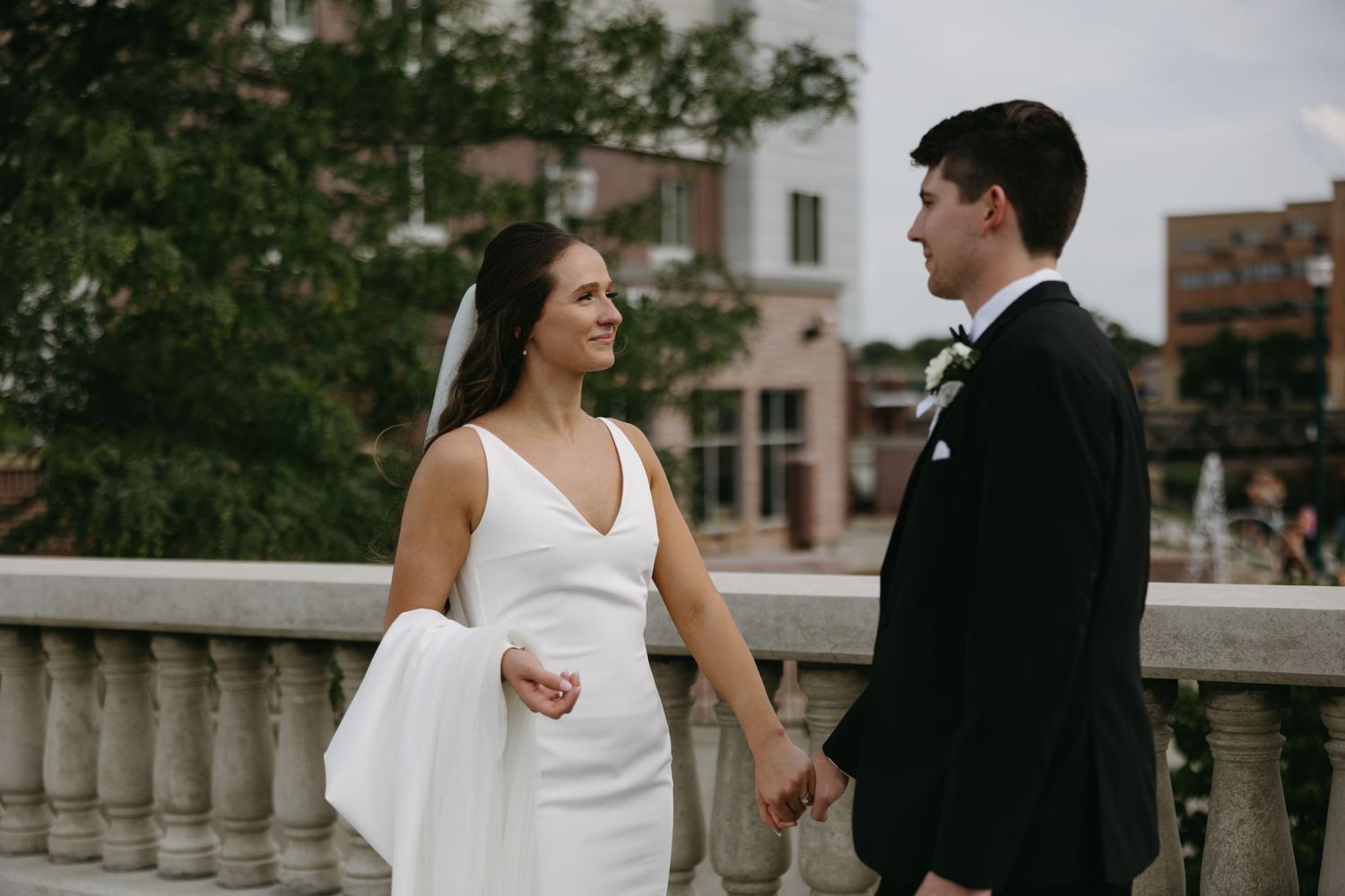 Couple shares intimate moment on stone balcony during urban wedding photoshoot.