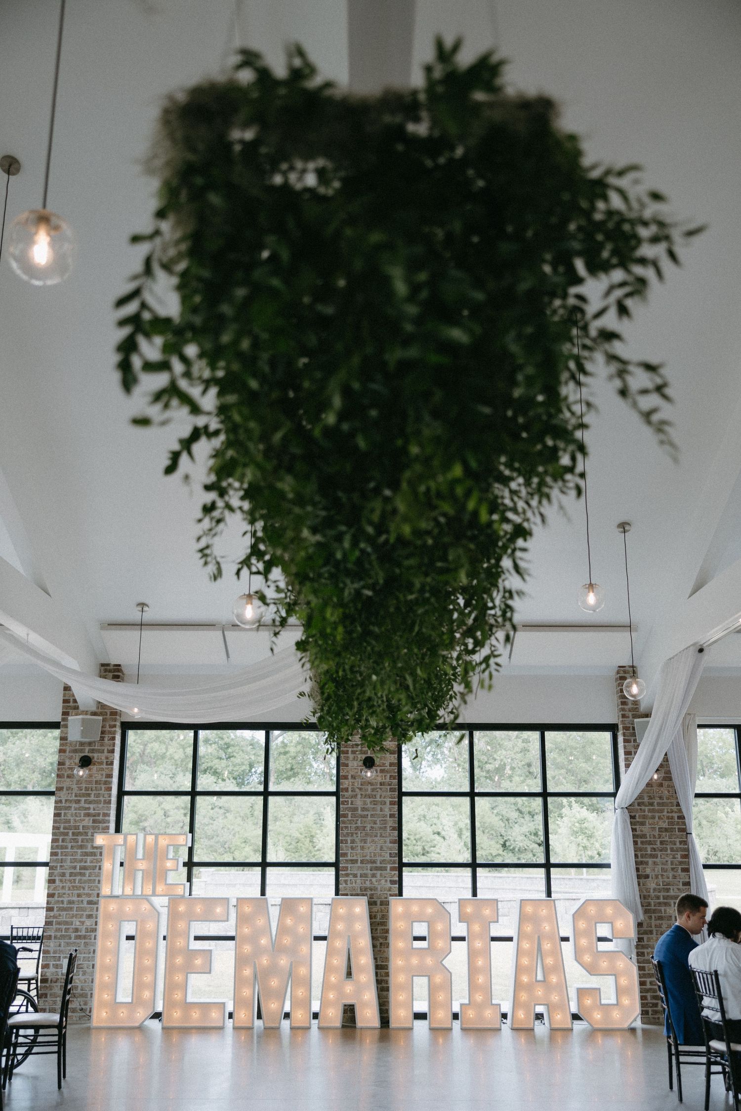 Modern wedding venue with dramatic greenery installation and illuminated 'The DeMarias' sign.