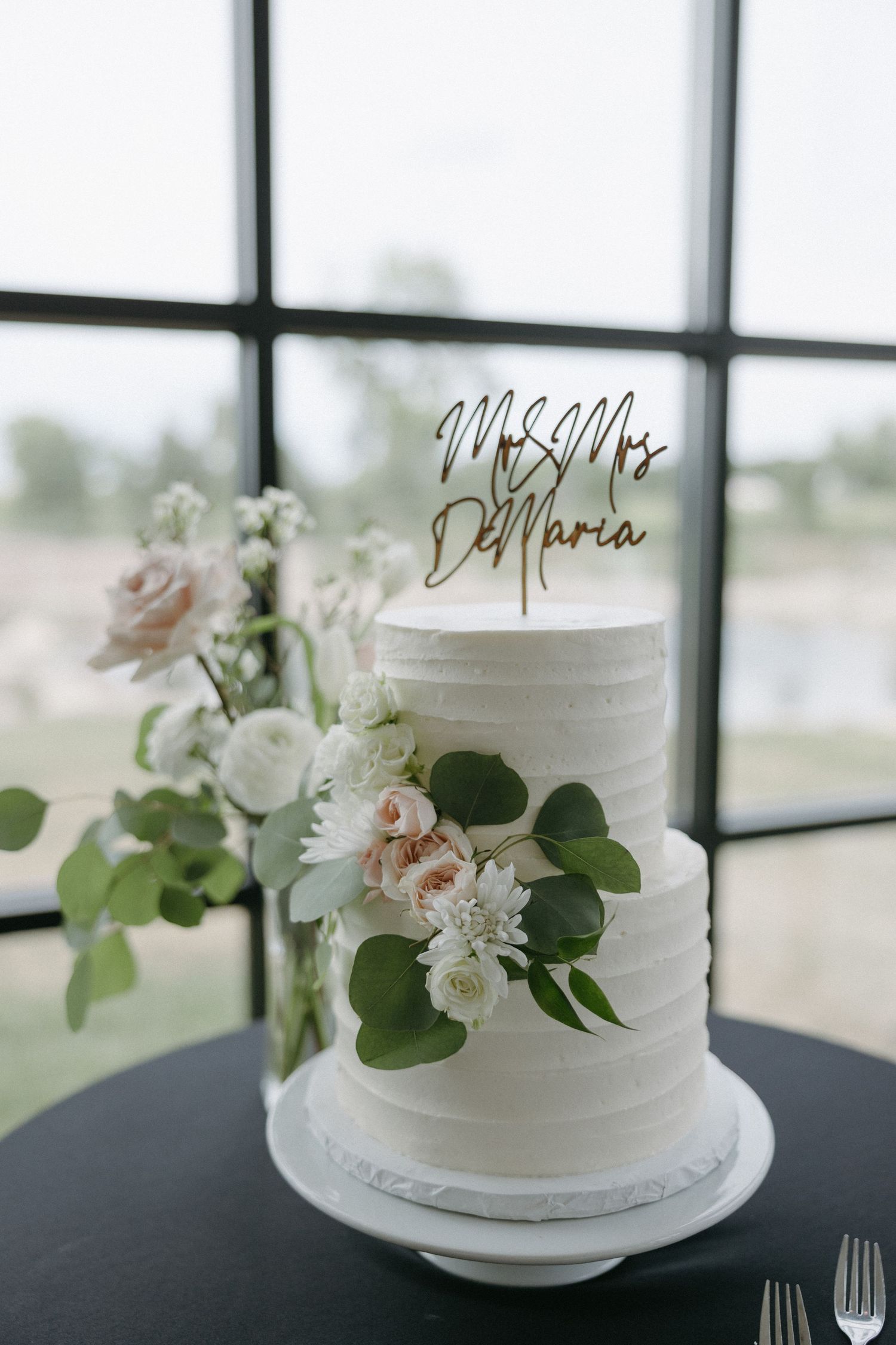 Elegant white wedding cake decorated with fresh flowers and a Mr & Mrs Maria gold topper.