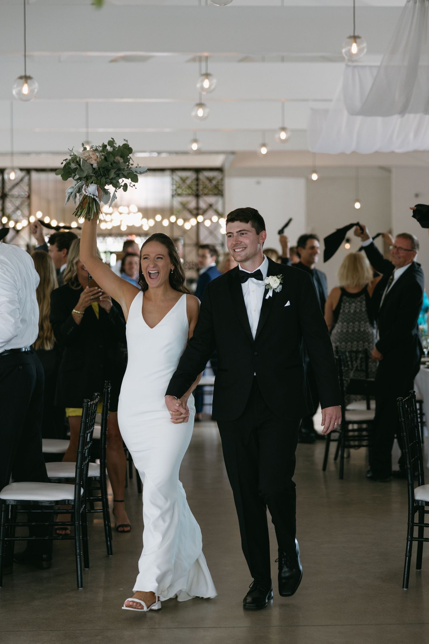 Couple shares their first dance under hanging greenery in bright reception venue.