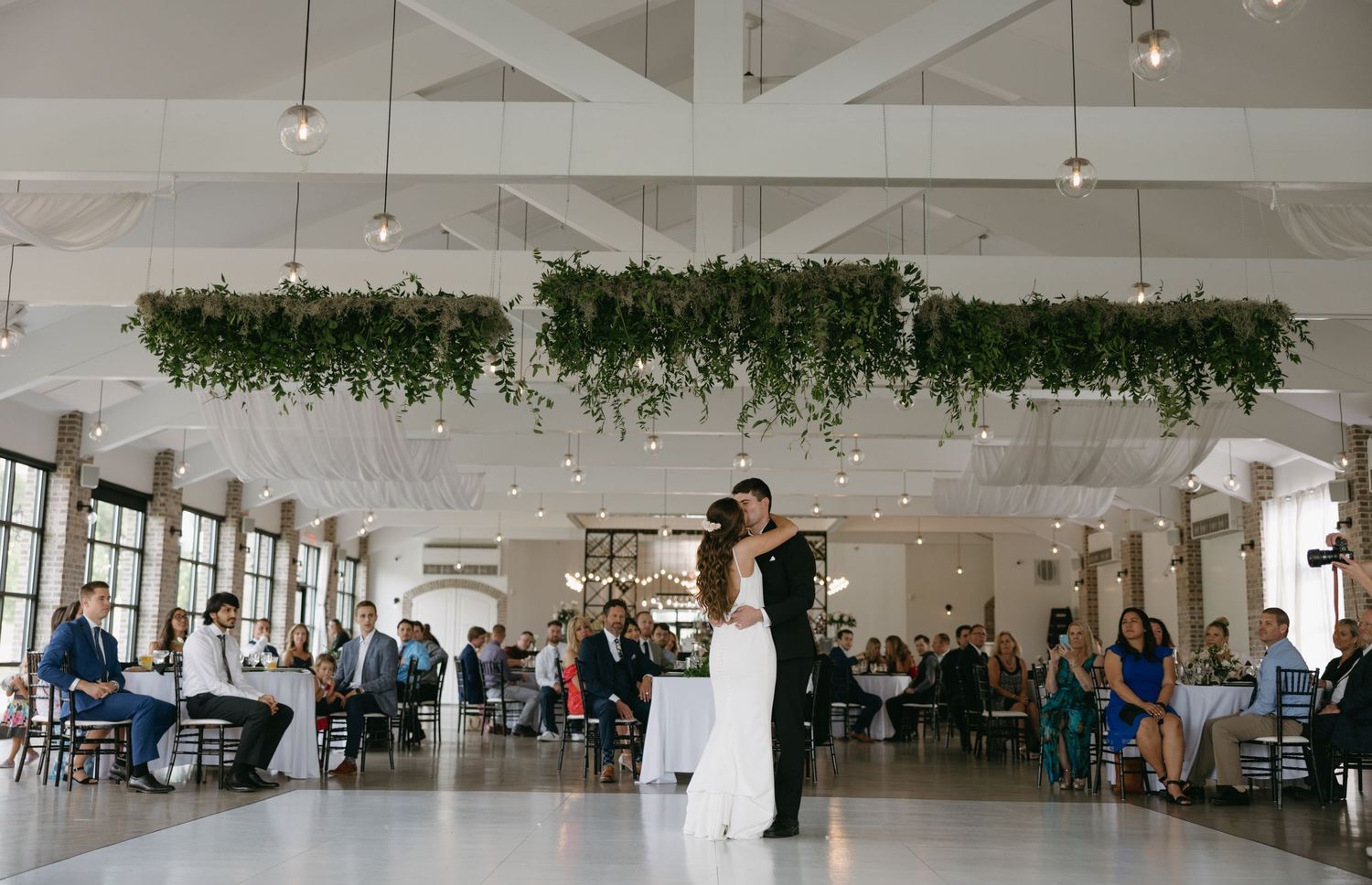 Couple dancing in an elegant venue with white decor and brick walls.