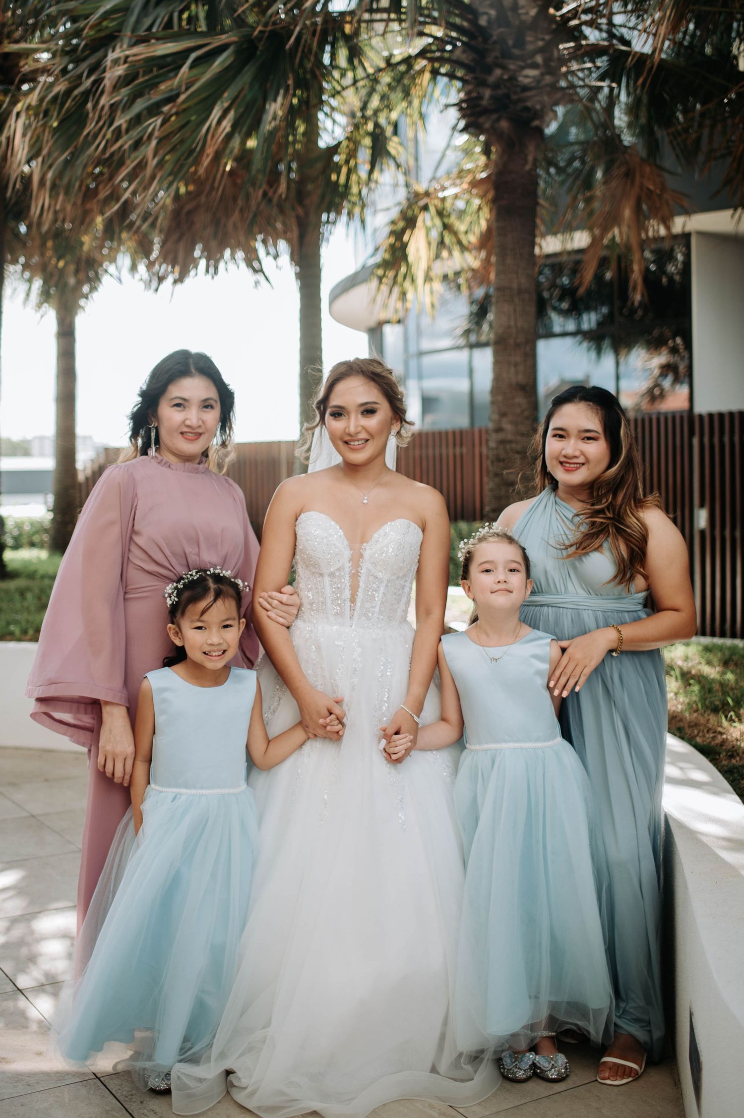 Wedding party in coordinating pastels and white gowns pose under palm trees.