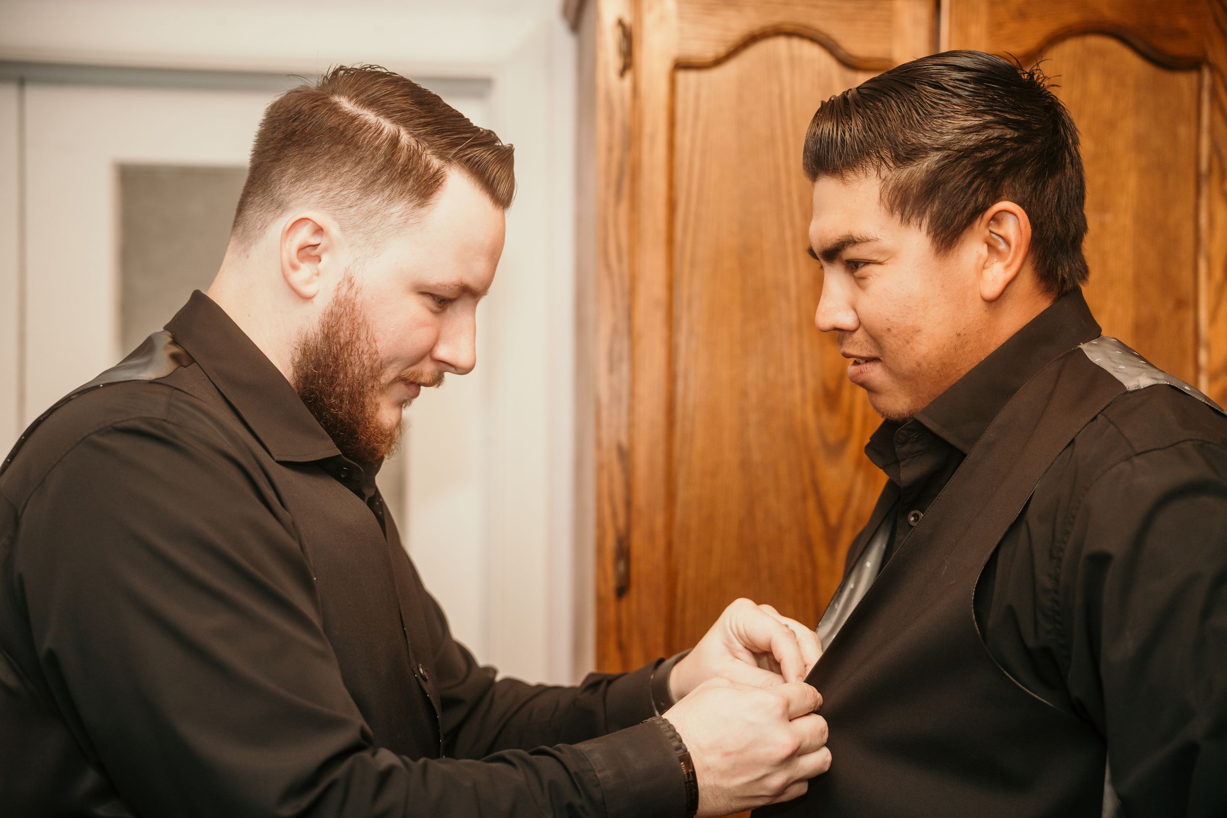 Two people in black formal attire helping each other prepare for an event.