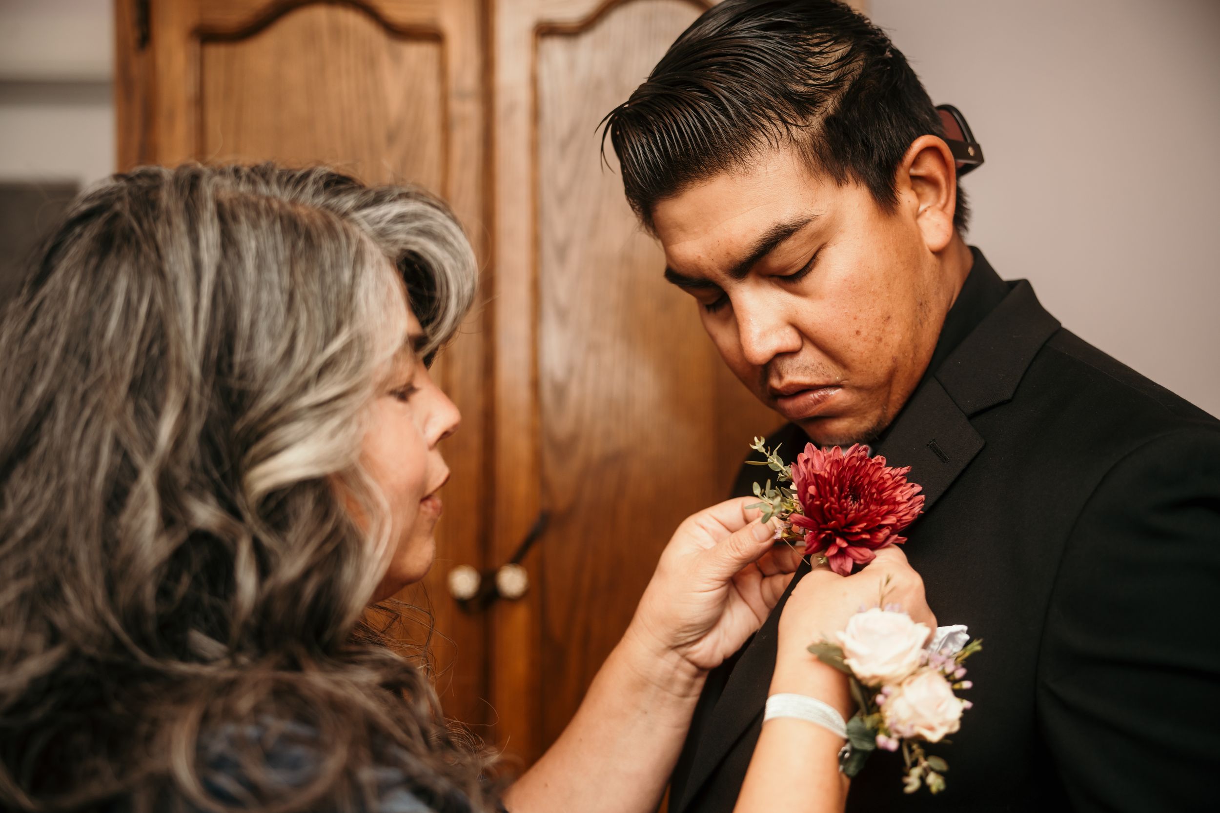 Close-up of hands pinning a red carnation boutonniere to a black suit lapel.