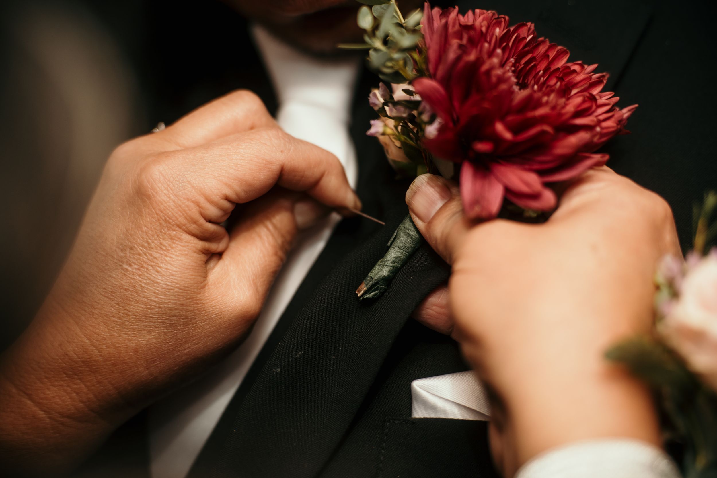 Hands pinning red carnation boutonniere onto black suit jacket.