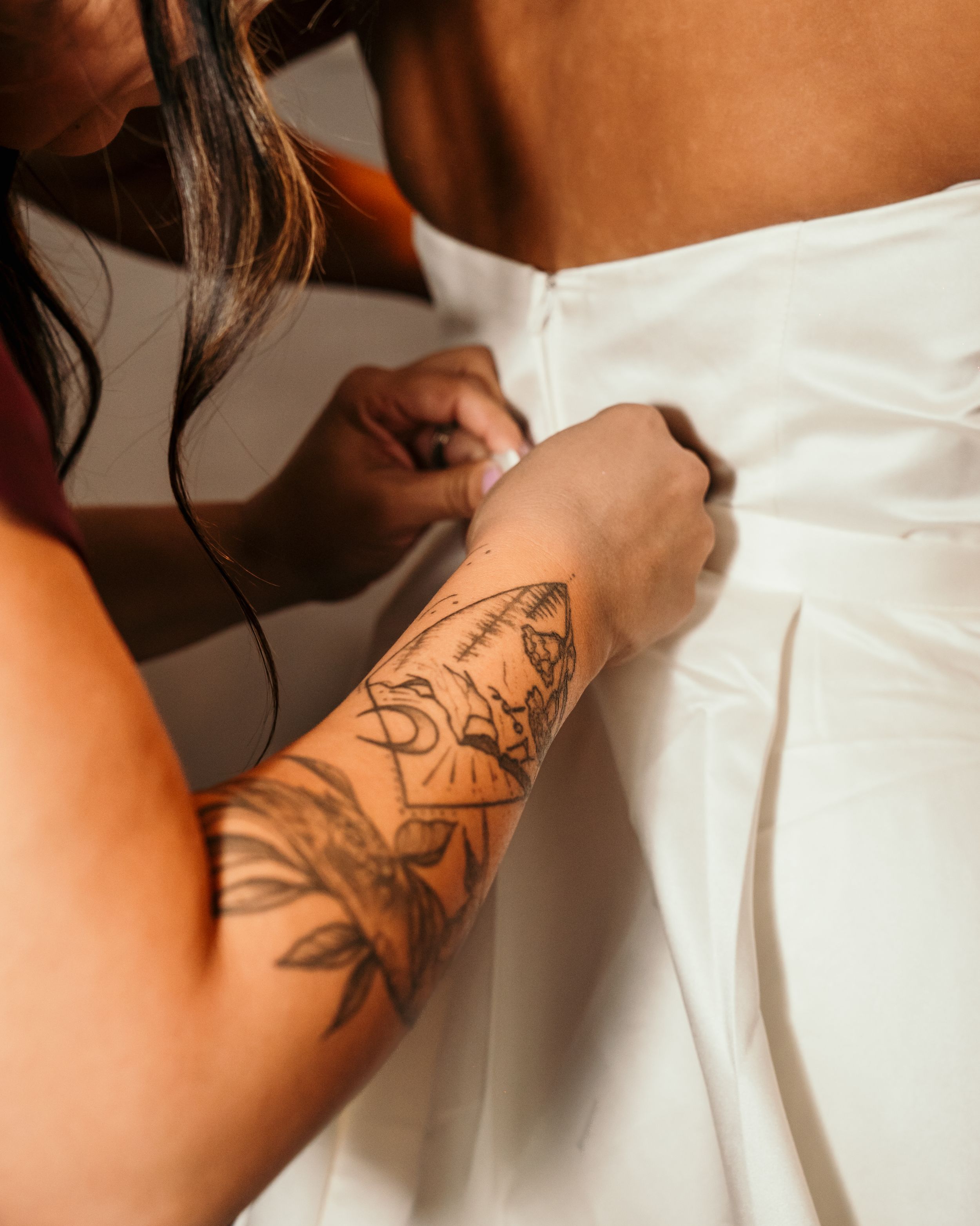 A tattooed arm adjusts a white wedding dress fabric during preparations.