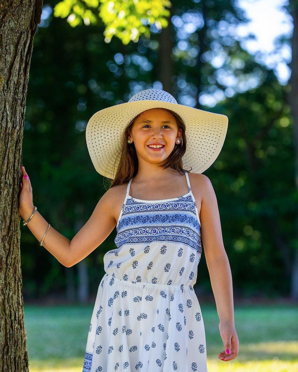 Summer portrait of person in sundress and straw hat leaning against tree.