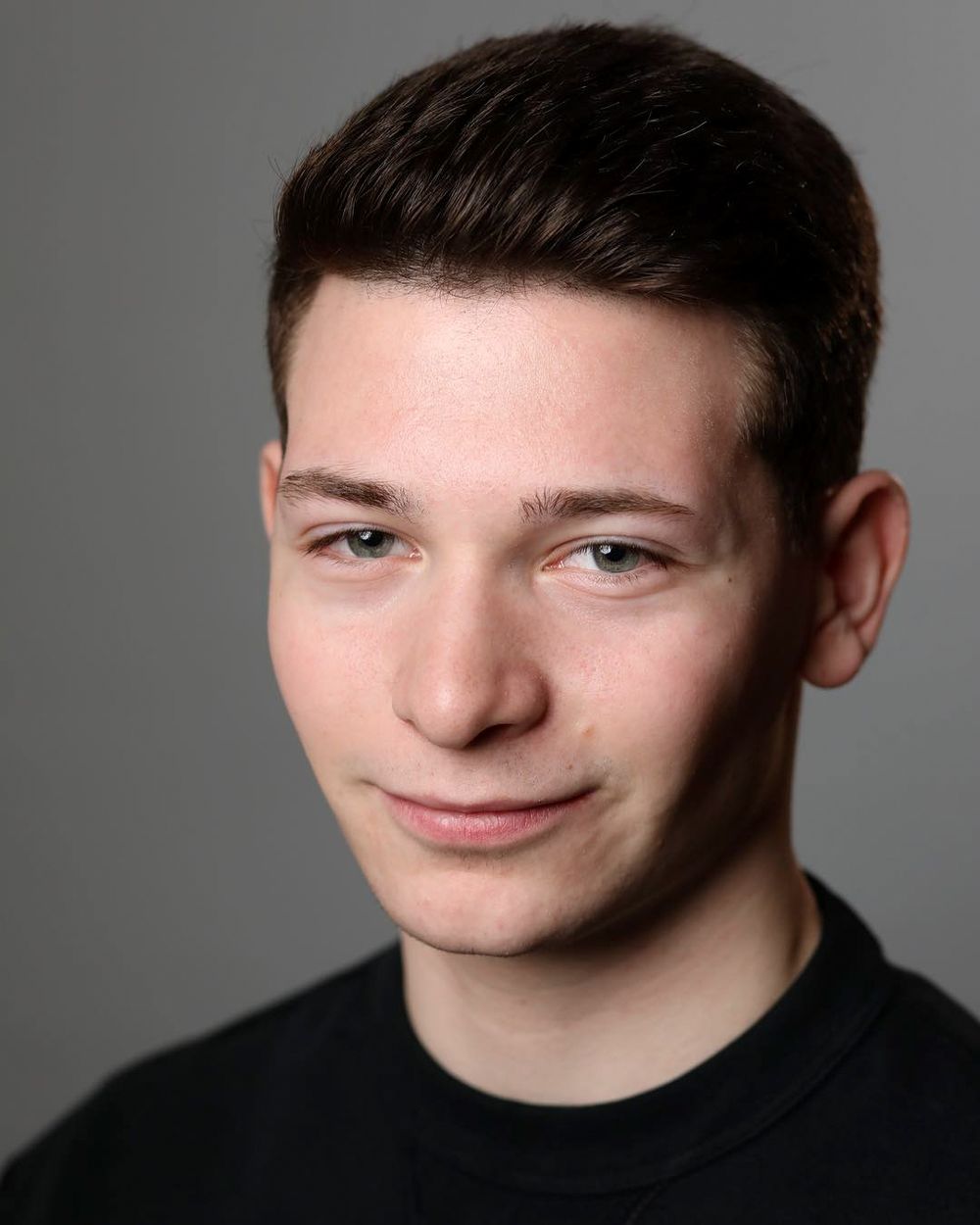 Studio headshot portrait of young person in black shirt against grey background.